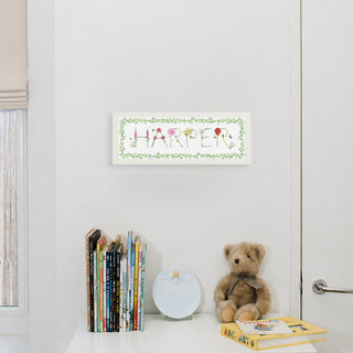 Custom Flower Name Print by The Letter Nest in flower letters spelling "Harper" with a vine border in a white frame hung up in a nursery