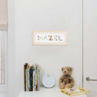 Shell Custom Name Print spelling "Hazel" in shell letter with scallop border, natural frame, hung up in nursery